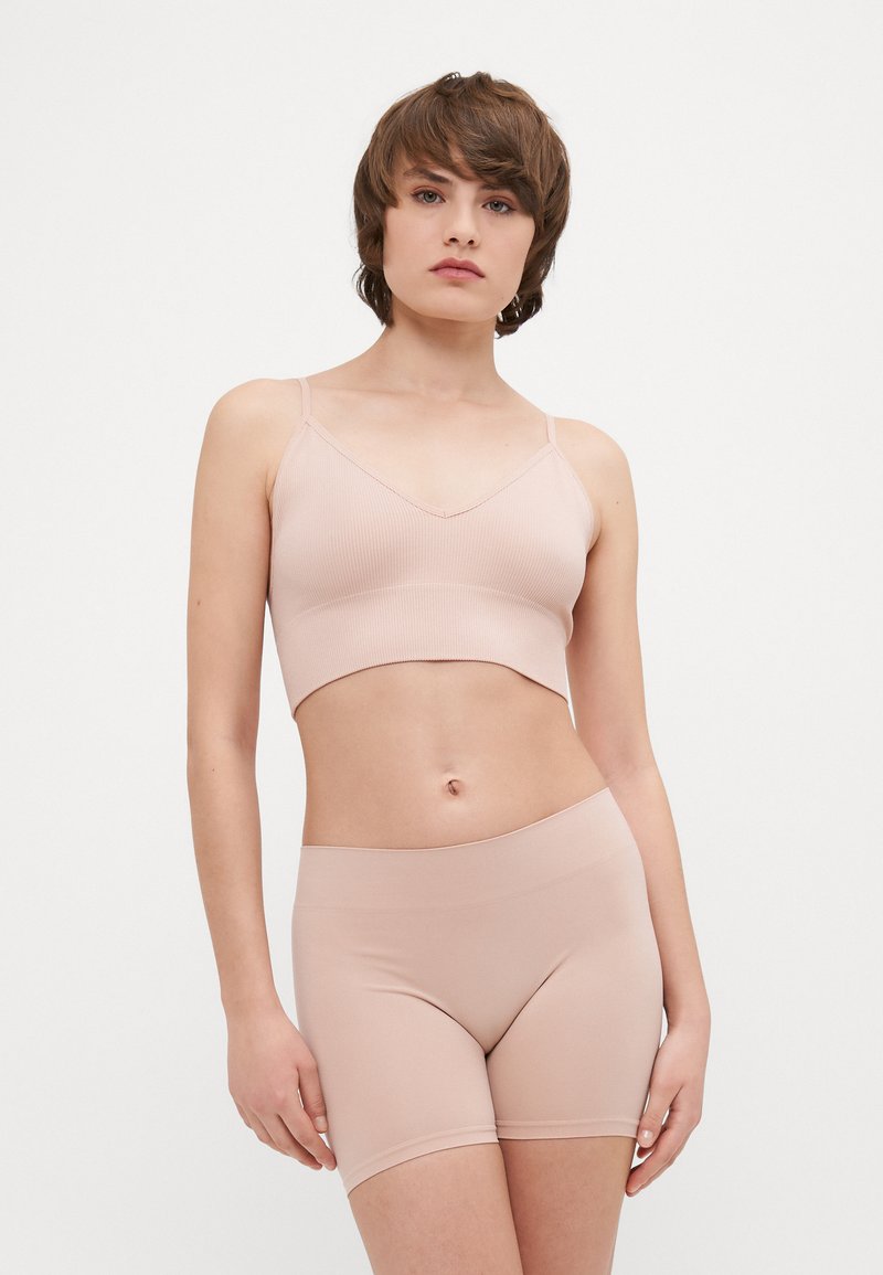 Rebrasti, svijetloružasti crop top i odgovarajuće kratke hlače od rastezljivog materijala. Top ima tanke naramenice i V-izrez; kratke hlače imaju elastičnu traku za struk.