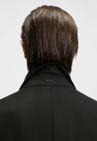 Giacca nera su misura con una finitura texturizzata, caratterizzata da un alto colletto e da un discreto dettaglio del logo "BOSS" sul retro.