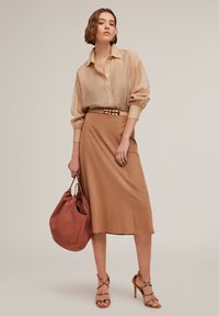 Beige overhemd met knopen en subtiele textuur, bruine midi-rok, bruine riem met metalen accenten, roze handtas met textuur en sandalen met bandjes.