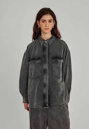 Gray denim shirt with a button-up front, pointed collar, and two chest pockets. Features a relaxed fit and visible stitching details.
