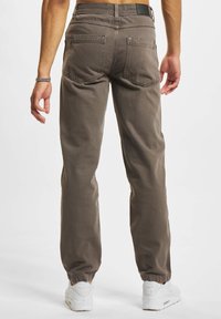 Pantaloni din bumbac maro, cu o croială tapered, având buzunare la spate, branhă pentru curea și mansete elastice, asortați cu pantofi sport albi.