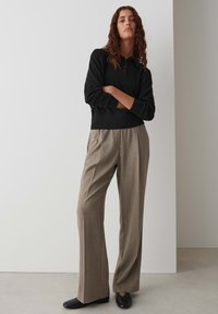 Schwarzes langärmliges Polohemd mit Kragen, kombiniert mit grauen karierten weit geschnittenen Hosen und schwarzen Slippern. Minimalistisches Design, weiche Textur.