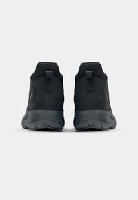 Black athletic shoes with a textured upper, padded collar, and sturdy rubber soles. Features include pull tabs on the heel and a sleek, minimalist design.