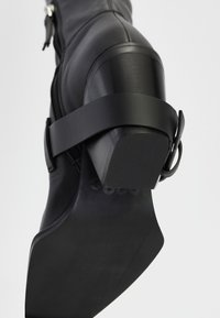 Black leather ankle boot featuring a zip closure, a matte finish, and a thick, squared heel with a strap detail around the ankle.