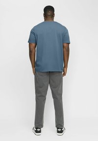 Camiseta azul de manga corta, material de algodón, corte relajado. Pantalones gris oscuro, diseño de pierna recta, textura sutil, combinados con zapatillas negras y blancas.