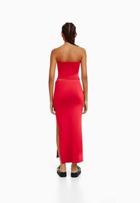 Robe midi rouge sans bretelles avec un corsage ajusté et une fente sur le côté. Fabriquée en tissu lisse, elle présente une silhouette élégante et un design minimaliste.