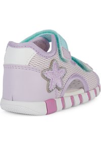 Zapatilla de malla en lavanda y blanco, con un acento de estrella, correa con gancho y bucle, y suela acolchada con detalles en rosa y blanco.