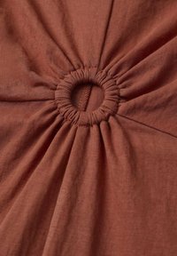 Tissu de couleur rouille avec un froncé circulaire au centre, créant un effet texturé et plissé autour de l'ouverture ronde. Texture lisse et douce.