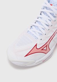 Λευκό αθλητικό παπούτσι με κόκκινες λεπτομέρειες και υφή στην ε�πιφάνεια. Διαθέτει κομψό σχεδιασμό, εμφανές πλαϊνό λογότυπο και διχτυωτό υλικό για διαπνοή.