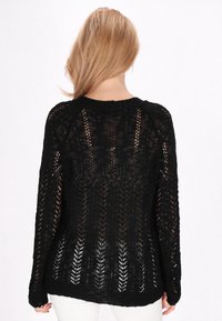 Maglione nero lavorato a maglia con un design a trama aperta, maniche lunghe e scollo rotondo, con polsini e orlo a coste. Tessuto testurizzato e leggero.