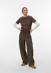 Καφέ κοντομάνικο μπλουζάκι φορεμένο πάνω από ένα λευκό μακρυμάνικο πουκάμισο, συνδυασμένο με χαλαρά παντελόνια χακί και πορτοκαλί ξύλινα παπούτσια. Απλός σχεδιασμός.