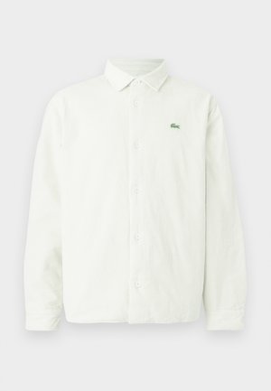 Gaiši zaļa kordurojas krekls ar garām piedurknēm, pogājamu priekšpusi, smailu apkakli un mazu zaļu Lacoste logotipu uz kreisā krūškurvja.