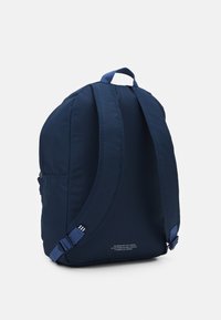 Marinblå ryggsäck med rundad form, i klädmaterial, vadderade axelremmar och ett handtag på toppen. Har en liten tryckt etikett på botten.