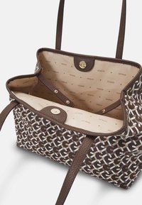 Sac fourre-tout à motifs marron avec intérieur beige. Extérieur à texture douce, arborant une impression de logo. Fermeture par un bouton-pression doré en haut.