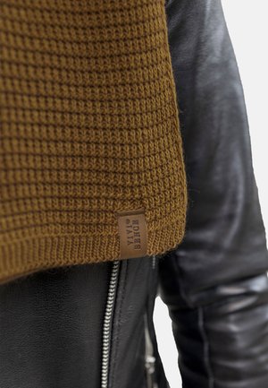 Maglione di lana marrone con motivo testurizzato, esposto accanto a una giacca di pelle nera con zip argentata e finitura liscia.