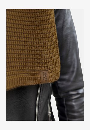 Suéter marrón de punto con patrón texturizado, mostrado junto a una chaqueta de cuero negra con cremallera plateada y acabado suave.