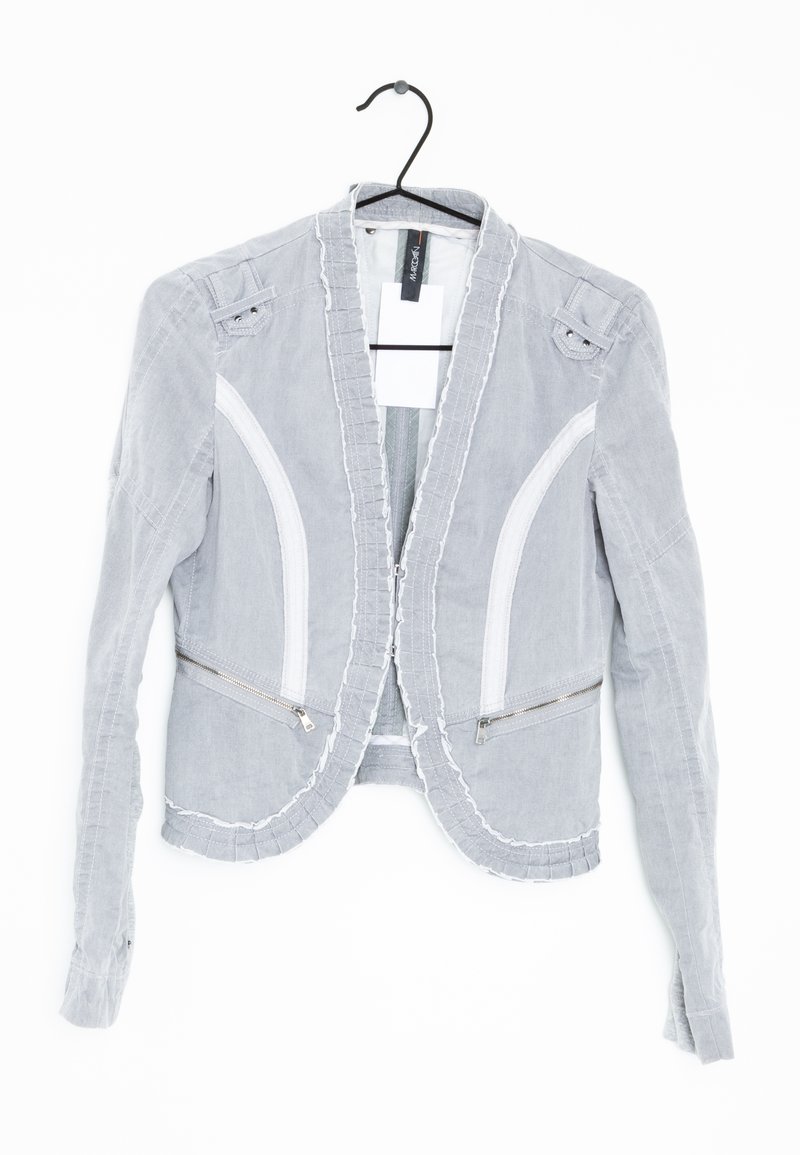 Veste blazer pour femmes gris clair avec surpiqûres blanches et poches zippées, suspendue sur un cintre noir contre un fond blanc.