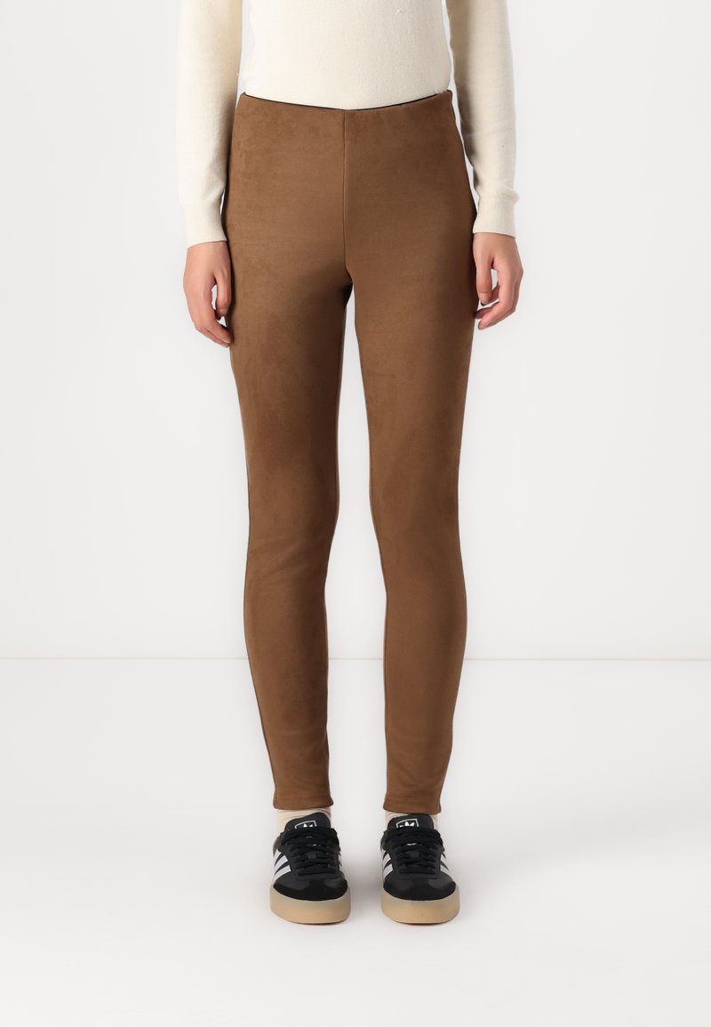 Leggings marroni elasticizzati con una texture liscia e opaca e vitino alto, abbinati a sneakers nere con strisce bianche e suola in gomma.