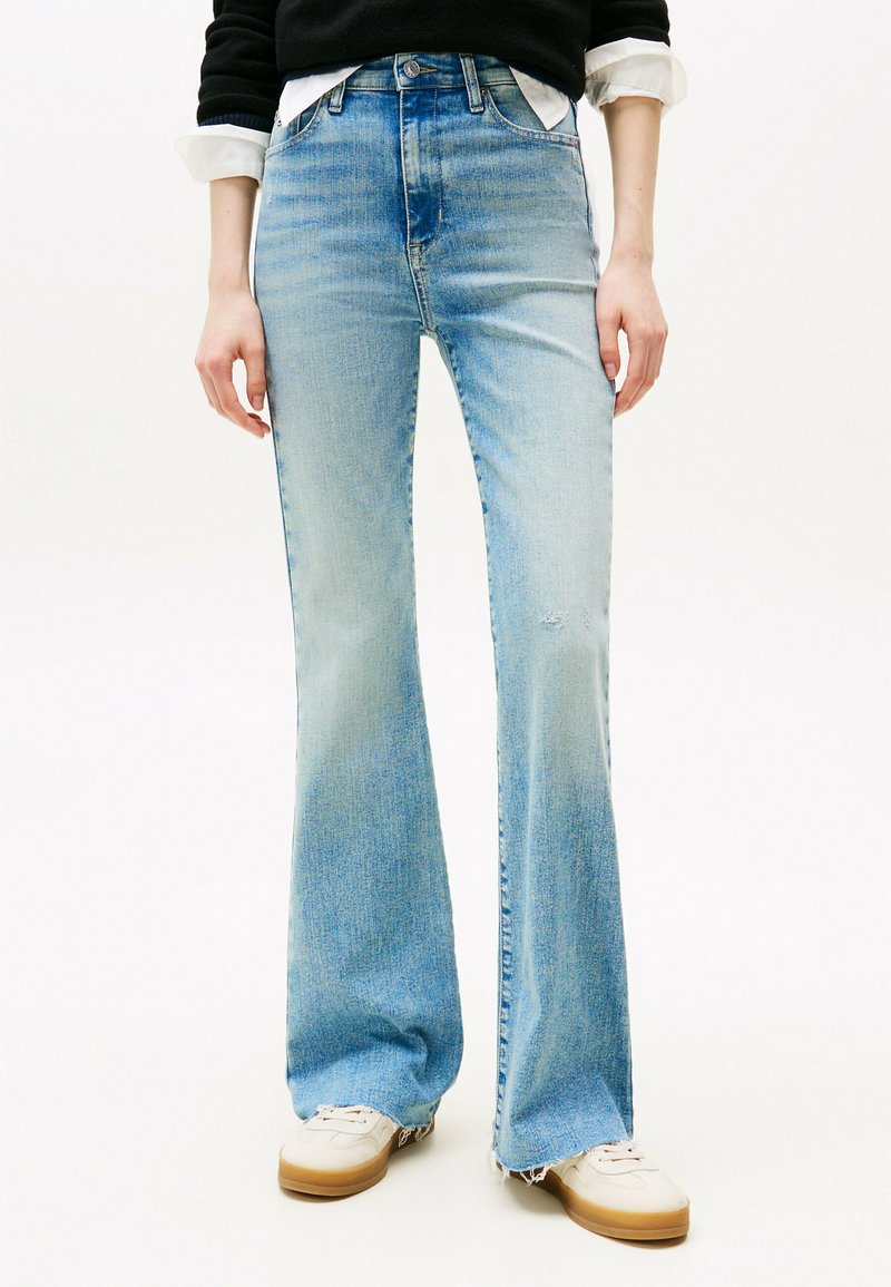 Jeans flare in denim azzurro con vita alta, caratterizzati da leggere scoloriture e orlo grezzo, abbinati a sneaker bianche.