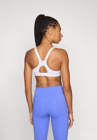 Witte sportbeha met verstelbare bandjes en een keyholedetail aan de achterkant, gecombineerd met hooggetailleerde blauwe leggings. Gladde textuur, minimalistische stijl.