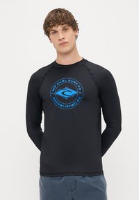 Czarna rashguard z długim rękawem, z niebieskim okrągłym logo z napisem "Rip Curl Surf Co" oraz "Established 69". Gładki, elastyczny materiał.