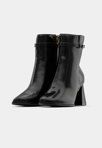 Mustad mustad mustad mustad, millel on terav nina, jäme konts ja õhuke rihm kuldse tooni kinnitusdetailidega.