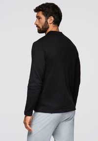 Maglietta nera a maniche lunghe con scollo rotondo, realizzata in un morbido tessuto textured. Presenta un orlo dritto e un design minimalista.