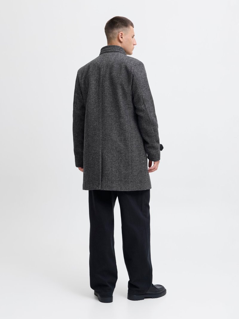 Abrigo de lana gris con un cuello alto, mangas largas y corte recto, combinado con pantalones oscuros y zapatos negros, visto desde atrás.