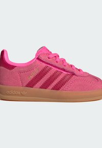 Baskets Adidas Gazelle roses avec dessus en daim, trois bandes rose plus foncé, lacets roses et semelle en caoutchouc couleur gomme sur fond blanc.