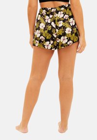 Shorts à imprimé floral avec un fond noir, mettant en avant des motifs de feuilles blanches et vertes, texture douce et ceinture élastique.