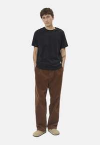 Čierne tričko s krátkym rukávom v kombinácii s hnedými zamatovými nohavicami a svetlohnedými nazúvacími topánkami. Jednoduchý, voľný strih a textúra.