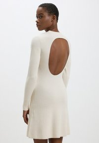 Abito a maniche lunghe, color crema, a coste con una ampia apertura rotonda sulla schiena e gonna fluente. Tessuto a maglia testurizzato con dettagli sottili.