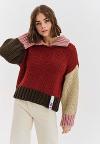 Wielokolorowy sweter dziany z szerokim kołnierzem, prezentujący odcienie czerwieni, brązu, różu i beżu. Charakterystyczna prążkowana faktura i dół.