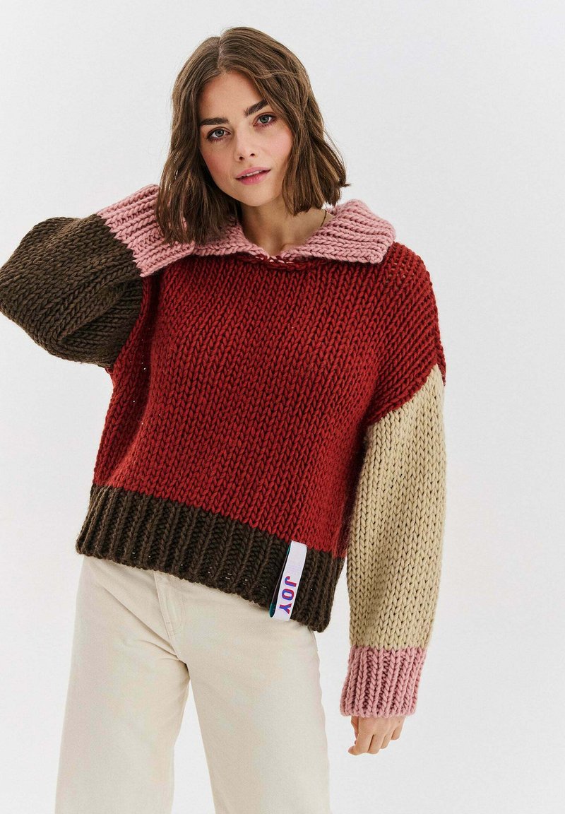 Wielokolorowy sweter dziany z szerokim kołnierzem, prezentujący odcienie czerwieni, brązu, różu i beżu. Charakterystyczna prążkowana faktura i dół.