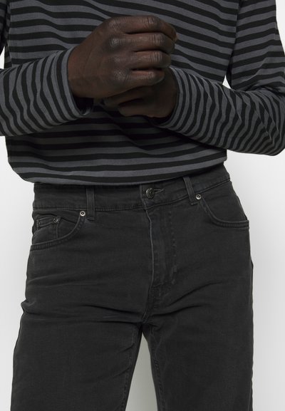 Jeans noirs à coupe slim, avec un design classique à cinq poches et une texture légèrement déchirée. Portés avec un haut à rayures sombres à manches longues.