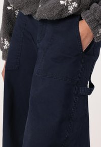 Calças cargo azul marinho feitas de algodão, com grandes bolsos laterais, um ajuste descontraído e uma cintura robusta com abas de ajuste lateral.