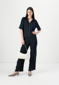 Navy textured dvoudílný outfit skládající se z košile s krátkým rukávem na knoflíčky a odpovídajících kalhot, doplněný bílou kabelkou a béžovými lodičkami.