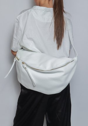 White leather sling bag with a curved shape, zip closure, and accent tie details. Smooth texture with gold hardware.