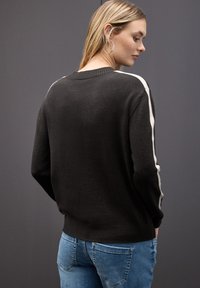 Czarny sweter z białymi bocznymi paskami, żebrowanym dekoltem i miękką teksturą, zestawiony z jasnoniebieskimi dżinsami, pokazany od tyłu.