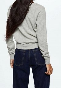 Szary sweter z dzianiny z okrągłym dekoltem, ściągaczami przy mankietach, zestawiony z ciemnoniebieskimi, wysokim stanem jeansami z wyraźnie zaznaczonymi tylnymi kieszeniami i przeszyciami.