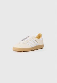 Witte leren sneaker met drie witte strepen, een beige tussenzool en een gestructureerde gumrubberen outsole. Beschikt over een vetersluiting en een zachte binnenvoering.