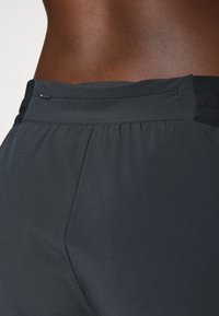 Schwarze sportliche Shorts aus einem glatten, leichten Material. Mit einem gerafften Taillenschnitt, dezenten Nähdetails und einem kleinen metallischen Akzent.