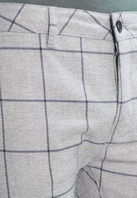 Szare spodnie z delikatnie teksturowanej tkaniny, z granatowym wzorem w kratę, przednią kieszenią i zapinane na guzik.