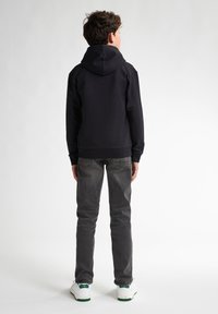 Felpa nera con cappuccio, polsini e fondo a coste, jeans grigi e sneakers bianche con dettagli verdi. Sfondo bianco puro.