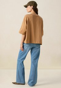 T-shirt oversize marron à manches courtes, associé à un jeans évasé bleu clair et une casquette de baseball à imprimé léopard. Texture de tissu lisse.