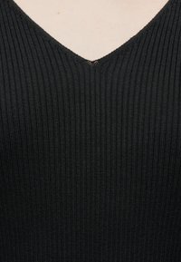 Μαύρο ριμπ πλεκτό ύφασμα με ντεκολτέ σε σχήμα V, που δείχνει υφή και λεπτομέρειες ραφής στο κέντρο του ντεκολτέ.