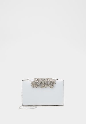 Biała prostokątna kopertówka z srebrnym kwiatowym zapięciem ozdobionym kamieniami i cienkim srebrnym paskiem łańcuszkowym na jednolitym tle.