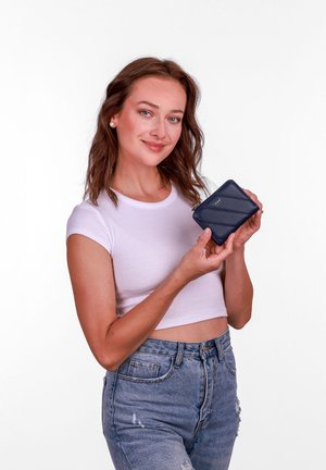 Navy zippered wallet with a chevron pattern, made of smooth leather, held by a person in a white top and distressed jeans against a plain background.