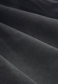 Tissu noir texturé avec des motifs subtils, affichant une surface lisse et un design en vagues repliées. Matériau doux et malléable.