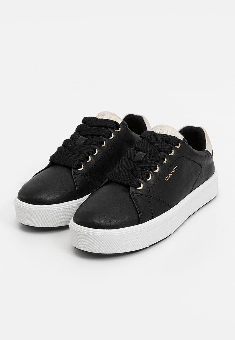 Sneakers in pelle nera con suola in gomma bianca, dotati di lacci prominenti, occhielli dorati e un accento crema sul tallone.